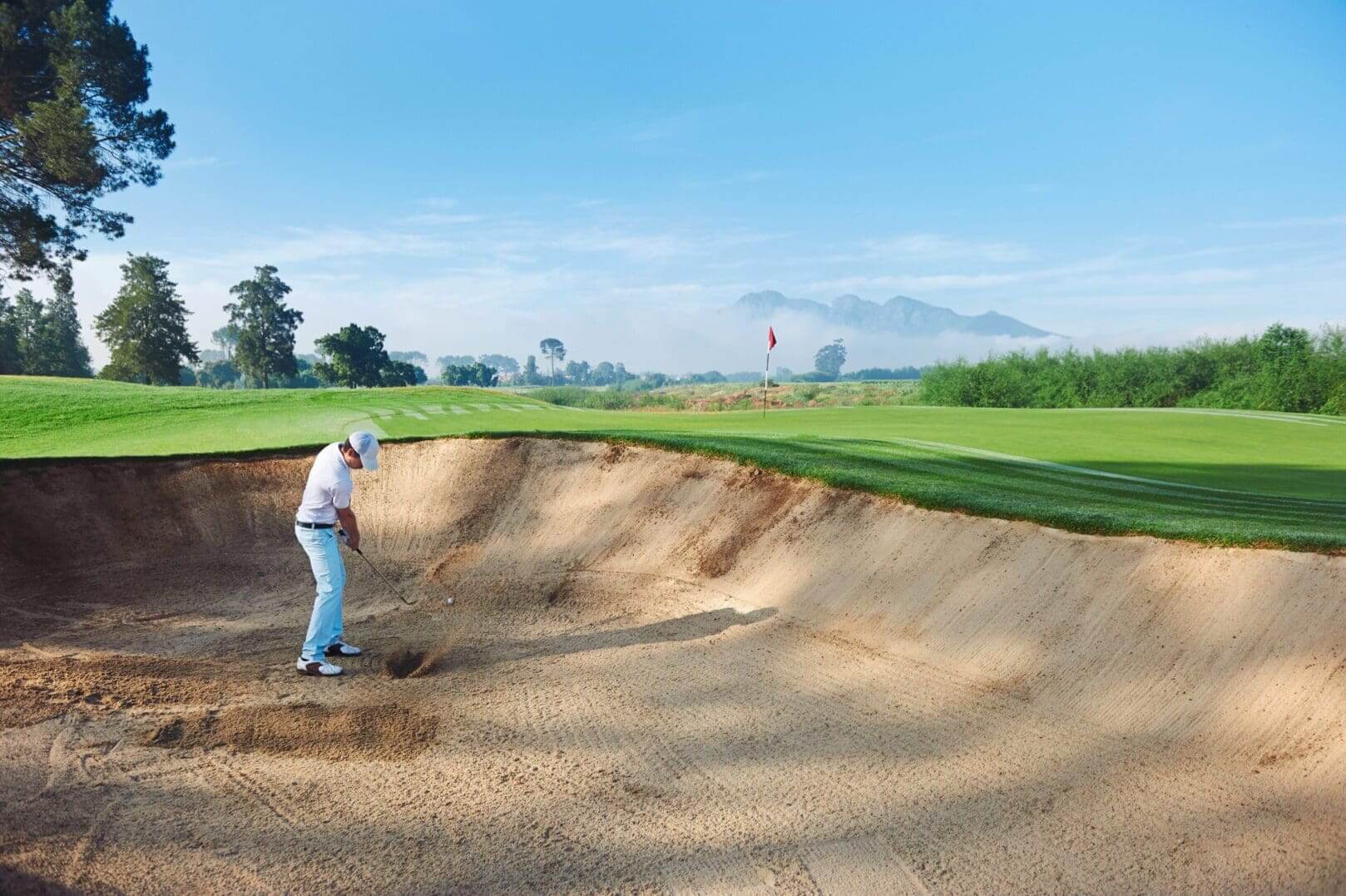 Golfer preparing to hit ball out of sand bunker on a sunny day.