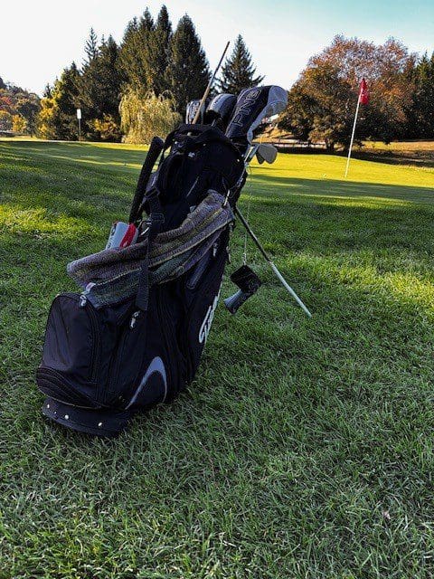 Golf bag with clubs and an umbrella on the grass.