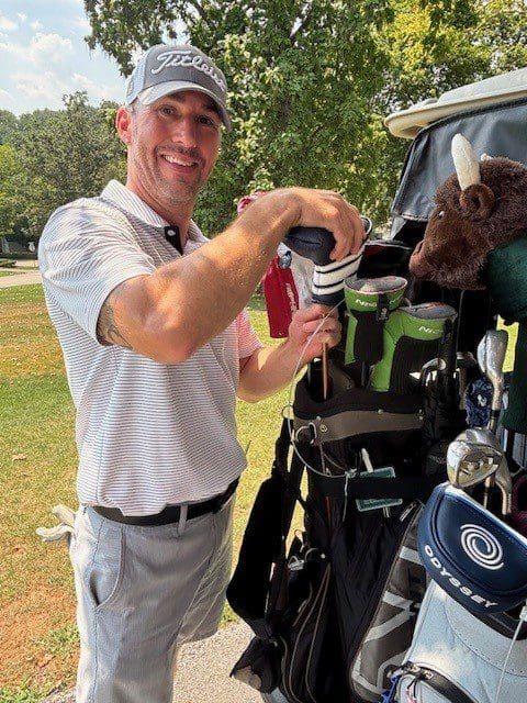 Man pouring a drink near golf clubs on a sunny day.