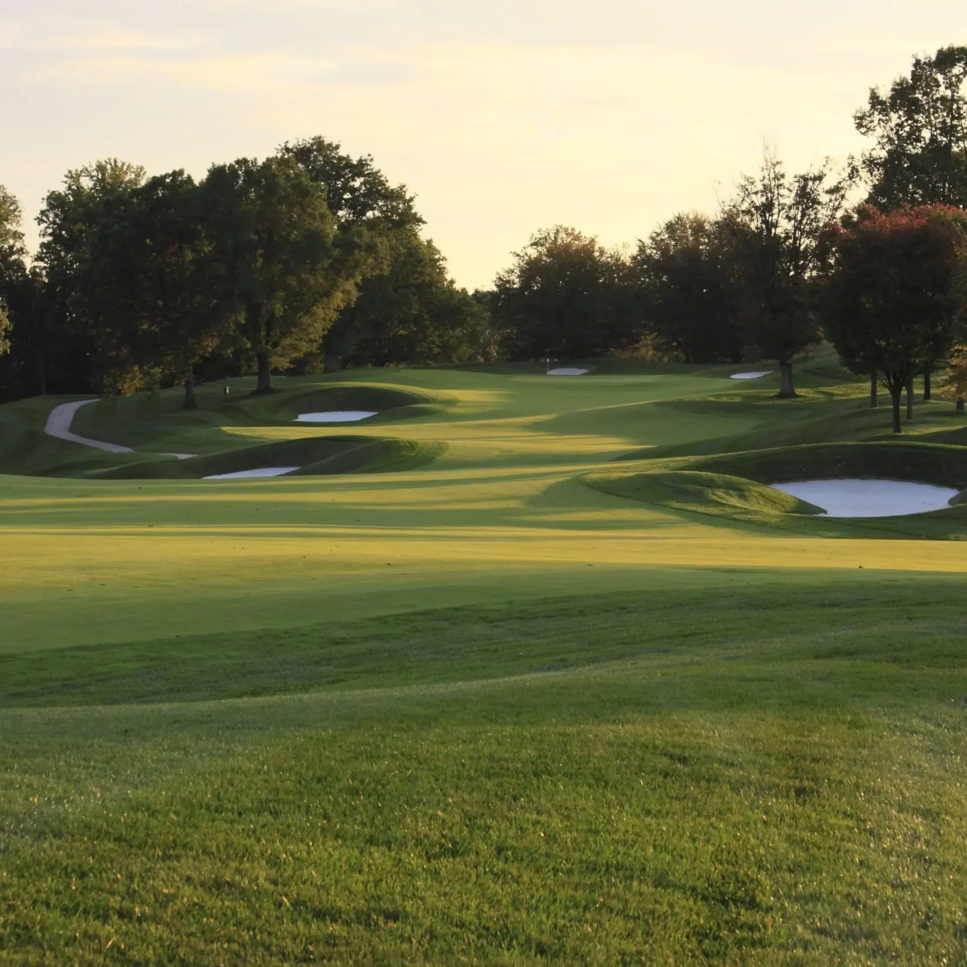 A serene golf course fairway with sand bunkers at sunset.