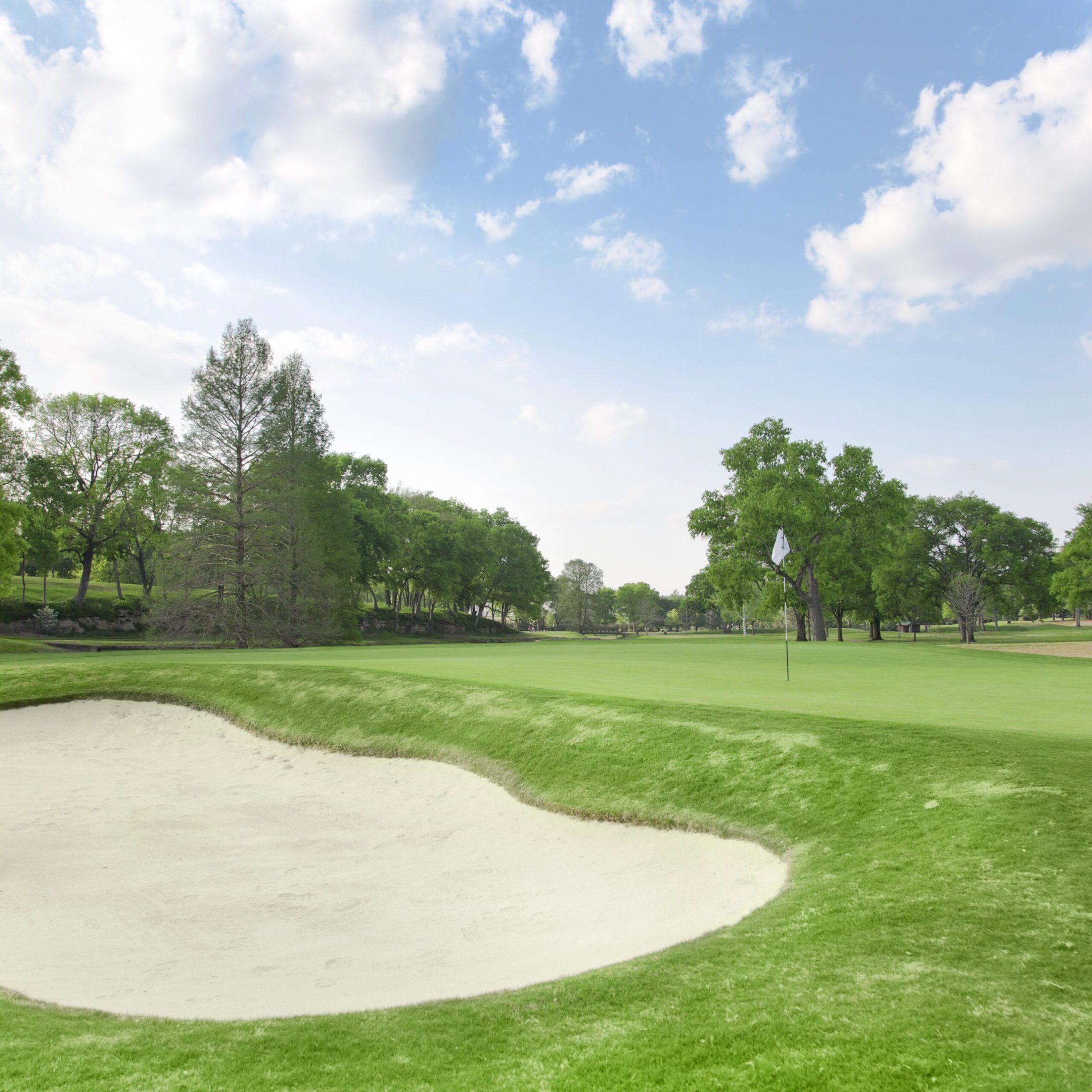 A scenic golf course with a sand bunker and green under a bright sky.